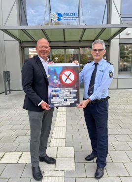 Landrat und Abteilungsleiter halten das Kampagnenplakat vor dem Polizeigebäude in Bergheim