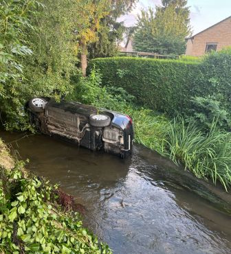 Auto liegt nach einem Verkehrsunfall seitlich in einem kleinen Fluss